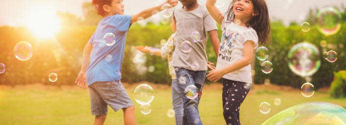 three young children playing with bubbles outside on grass