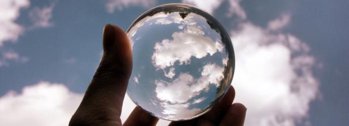 A person holding up a small magnifying glass into the sky 