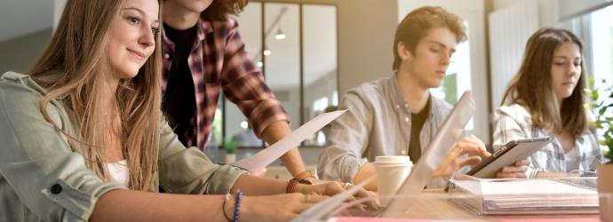 four students sitting at a desk with notepads