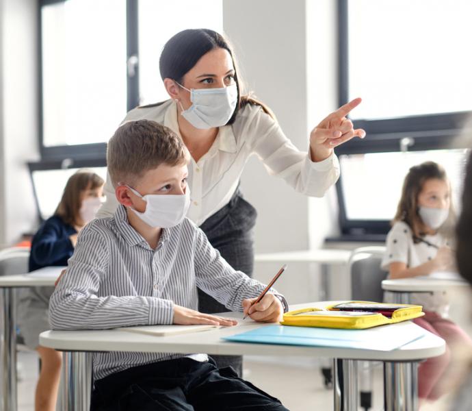 Female teacher supporting male pupil - both are wearing masks in the classroom