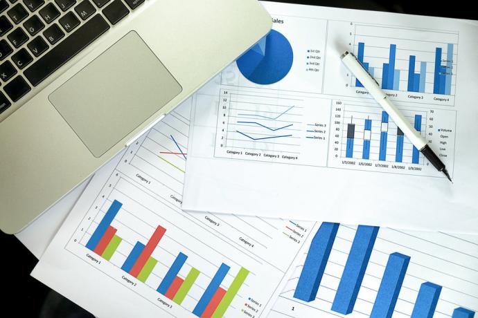 Paperwork with charts and graphs on a table with a laptop