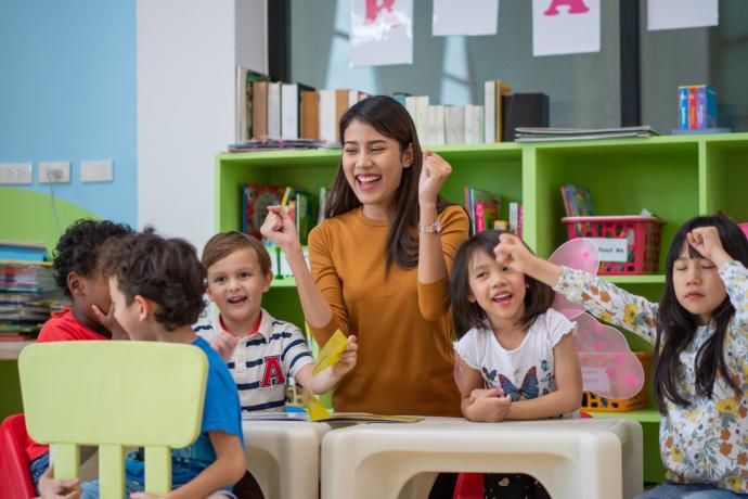 5 primary school aged pupils and female teacher sitting around a table in a colourful classroom