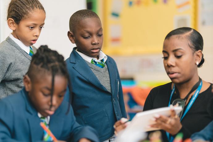 Image shows a teacher helping primary aged children read through some instructions for an activity