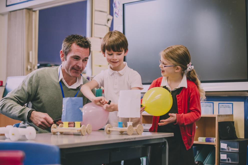 Male teacher supporting two primary school children in a lesson